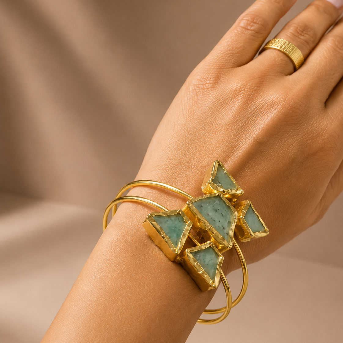 Gold bracelet with green gemstones on a hand against a beige background