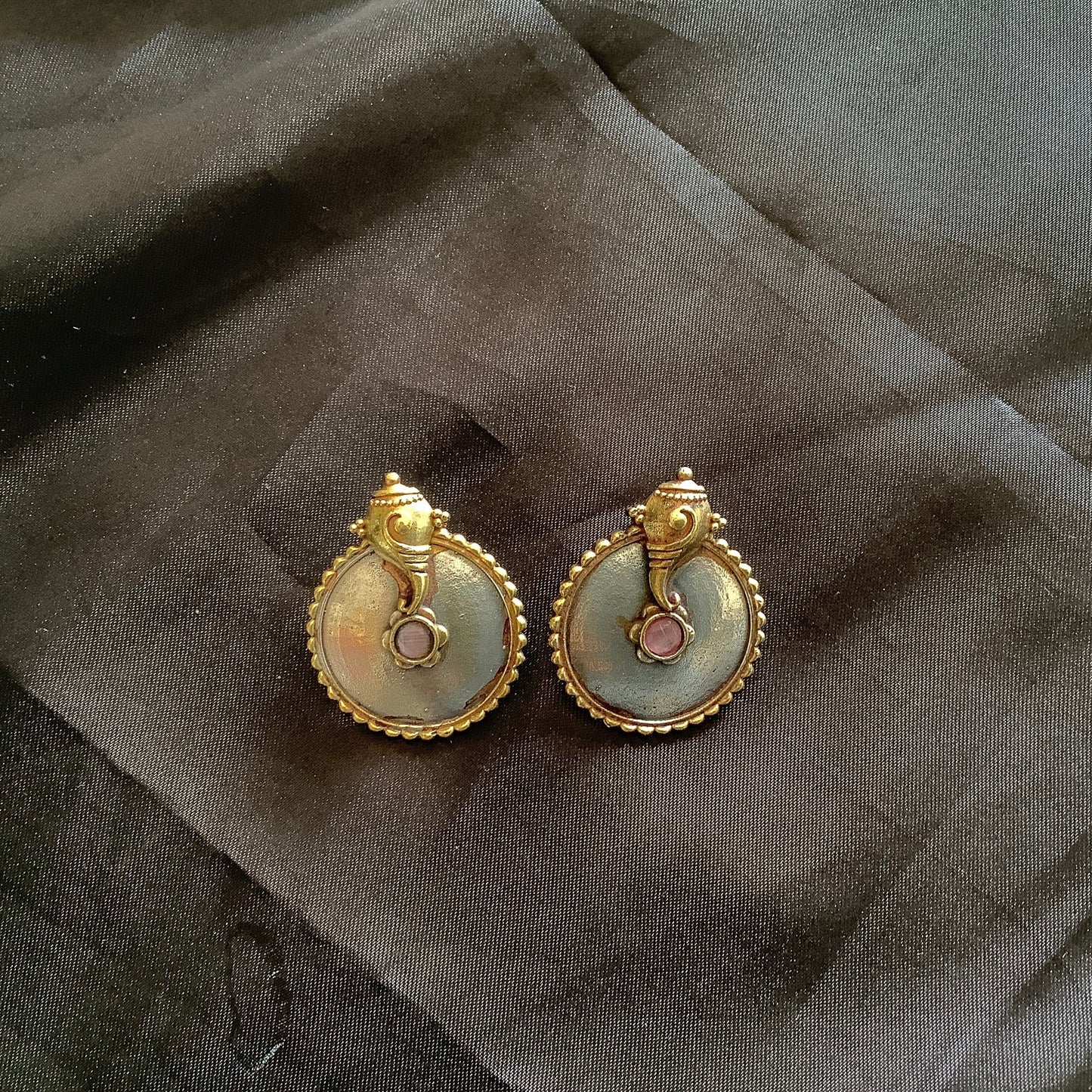 Pair of gold and gemstone earrings on a dark fabric background