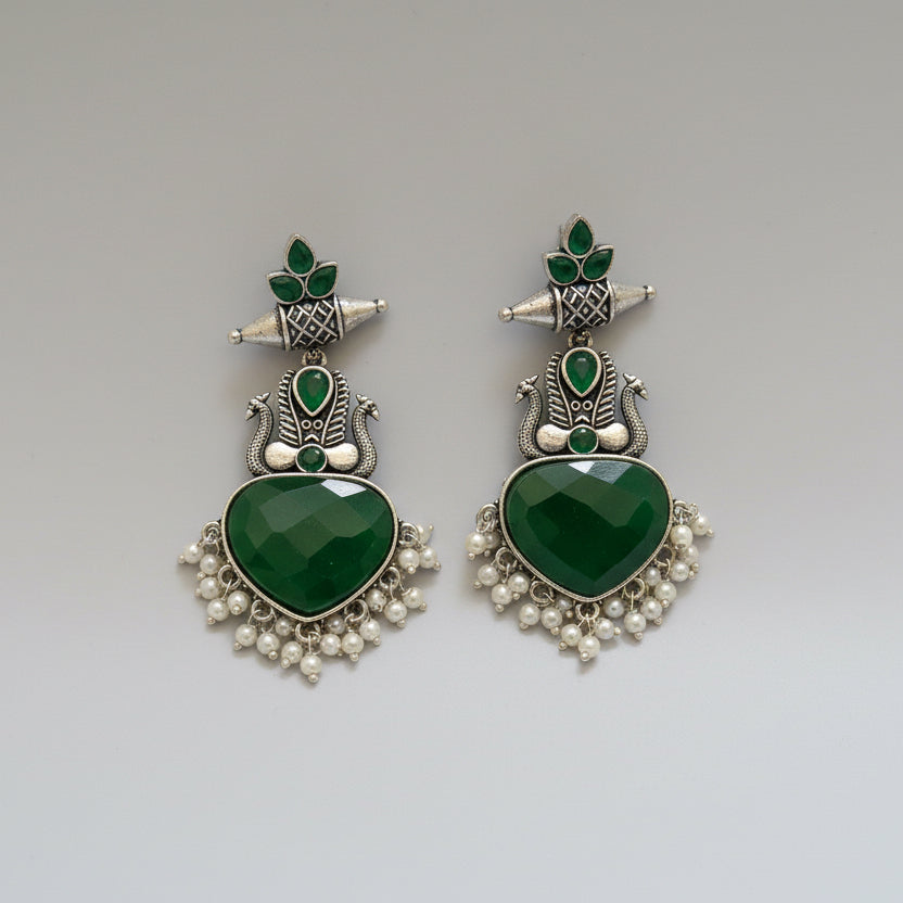 Pair of green heart-shaped earrings with silver and green accents on a black fabric background