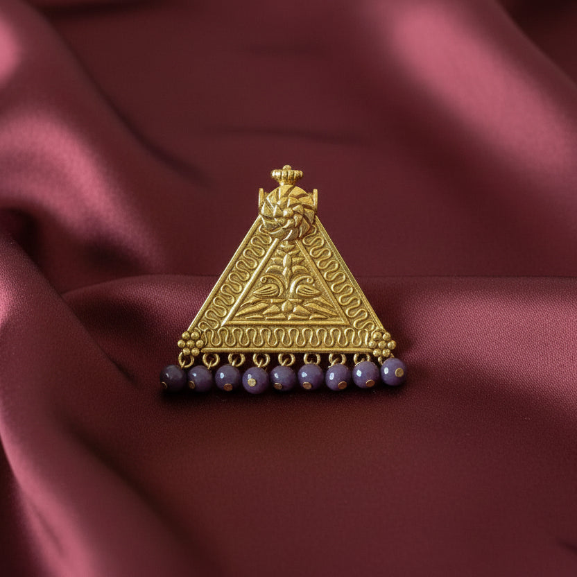 Decorative gold triangle pendant with purple beads on a black fabric background