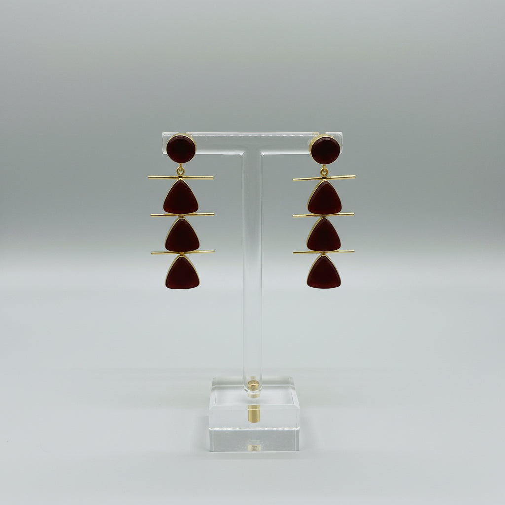 Pair of earrings with gold and red design on a dark surface