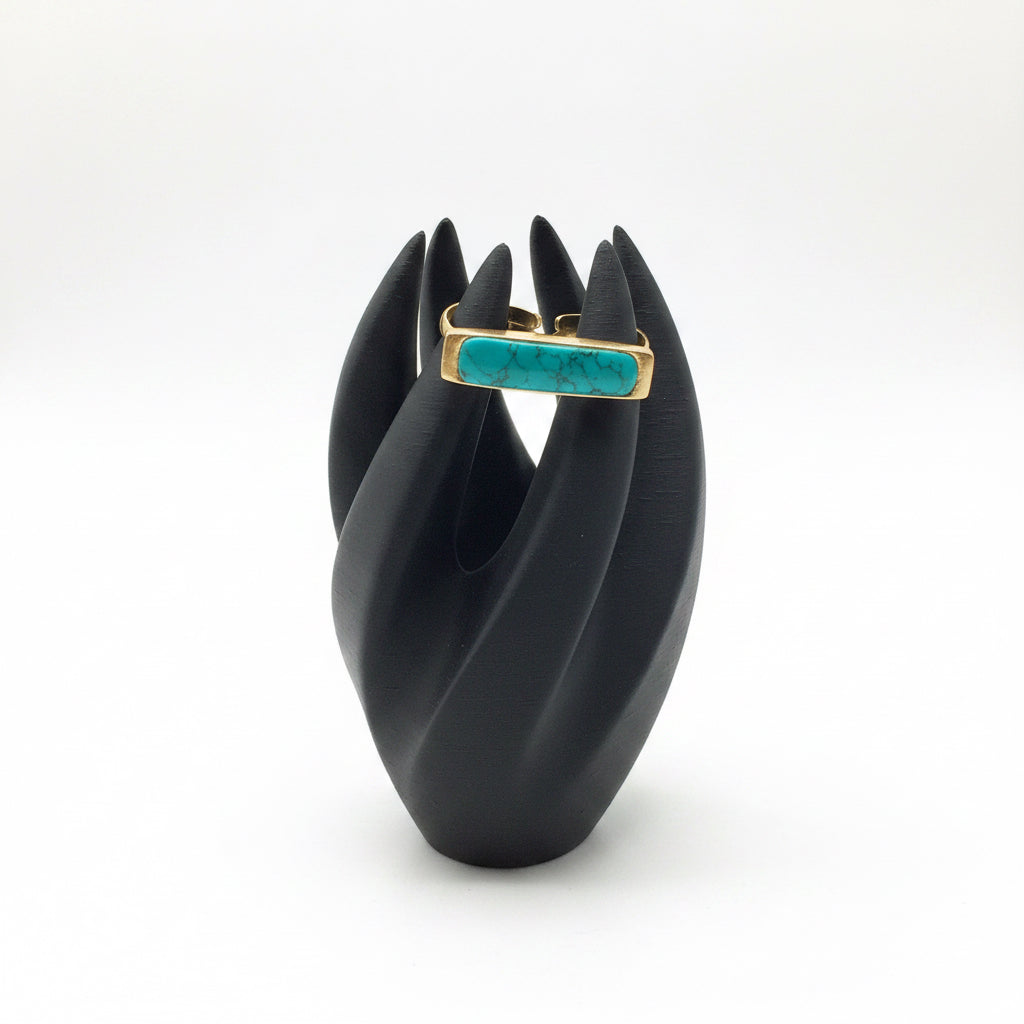Teal ring with gold band on a black stand against a sheet music background
