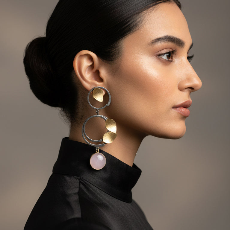 Pair of earrings with gold and silver components on a gray card against a dark background