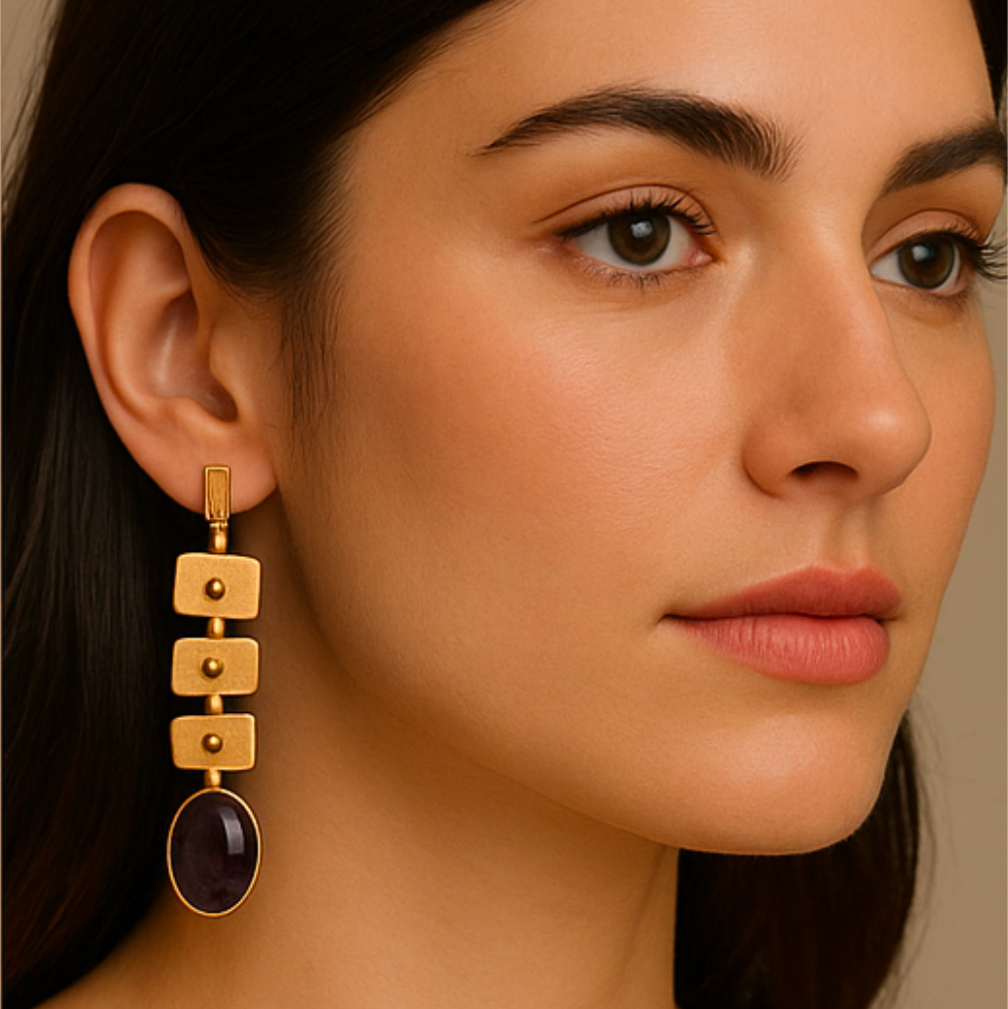 Close-up of a woman wearing gold earrings with a dark stone on a neutral background