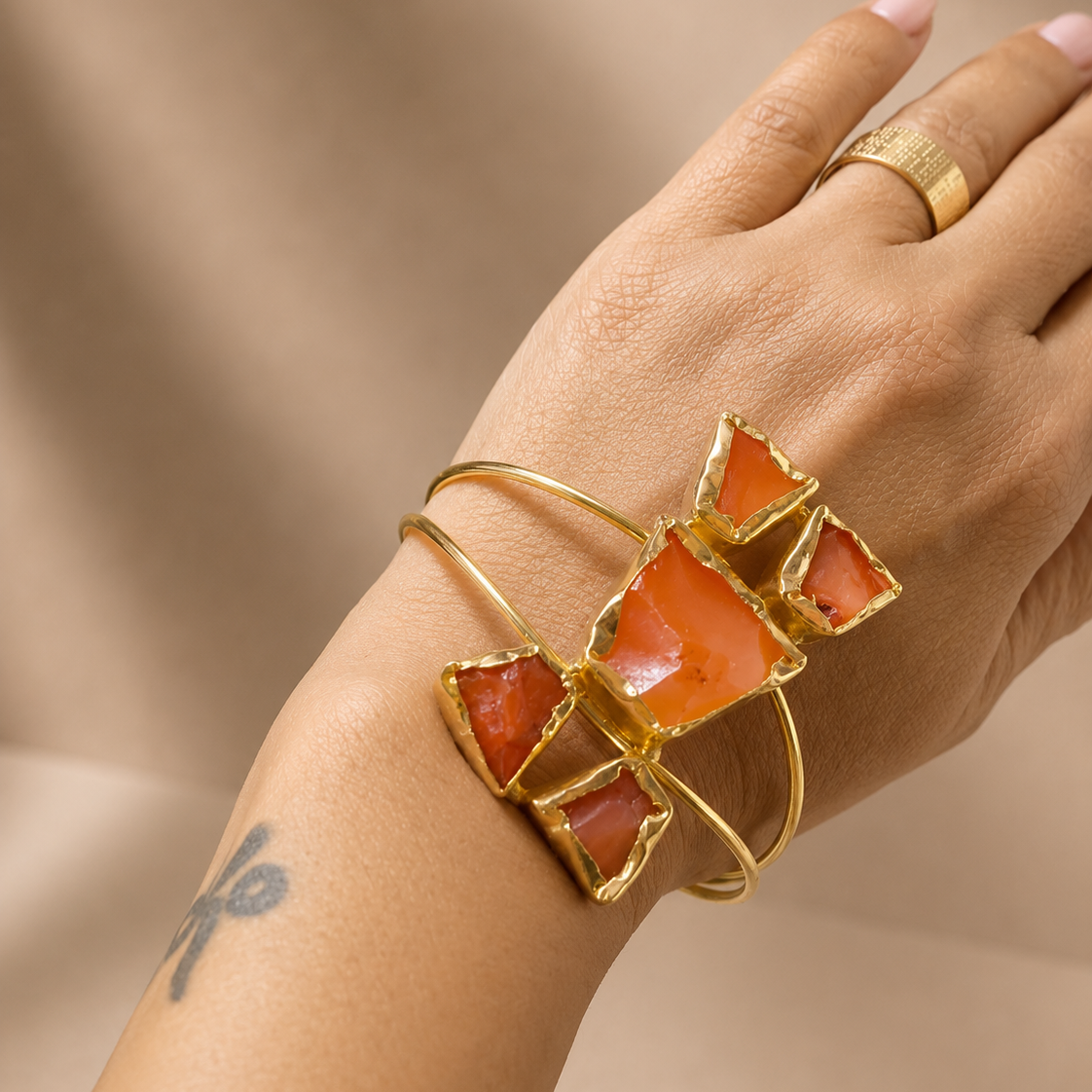 Hand wearing a gold bracelet with red stones on a beige background