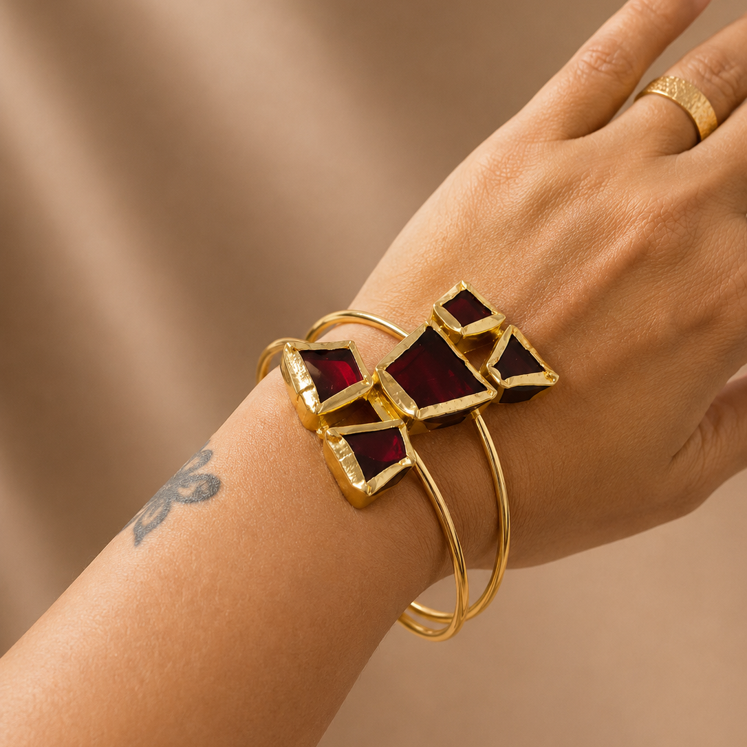 Gold bracelet with red gemstones on a wrist against a beige background