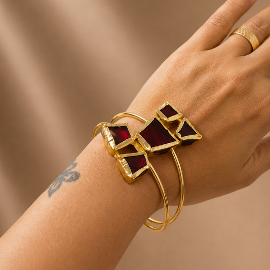 Gold bracelet with red gemstones on a wrist against a beige background