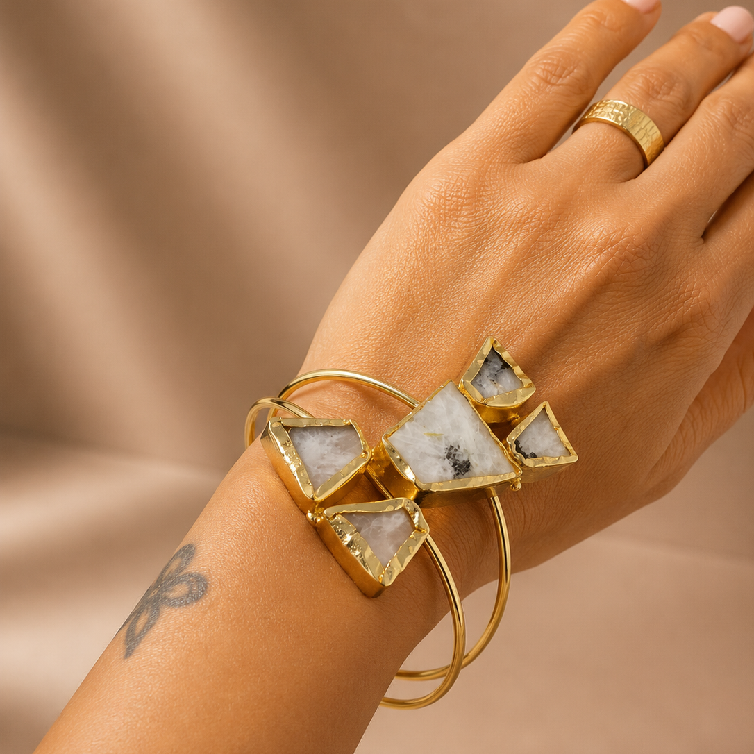 Hand wearing a gold bracelet with triangular gemstones on a beige background