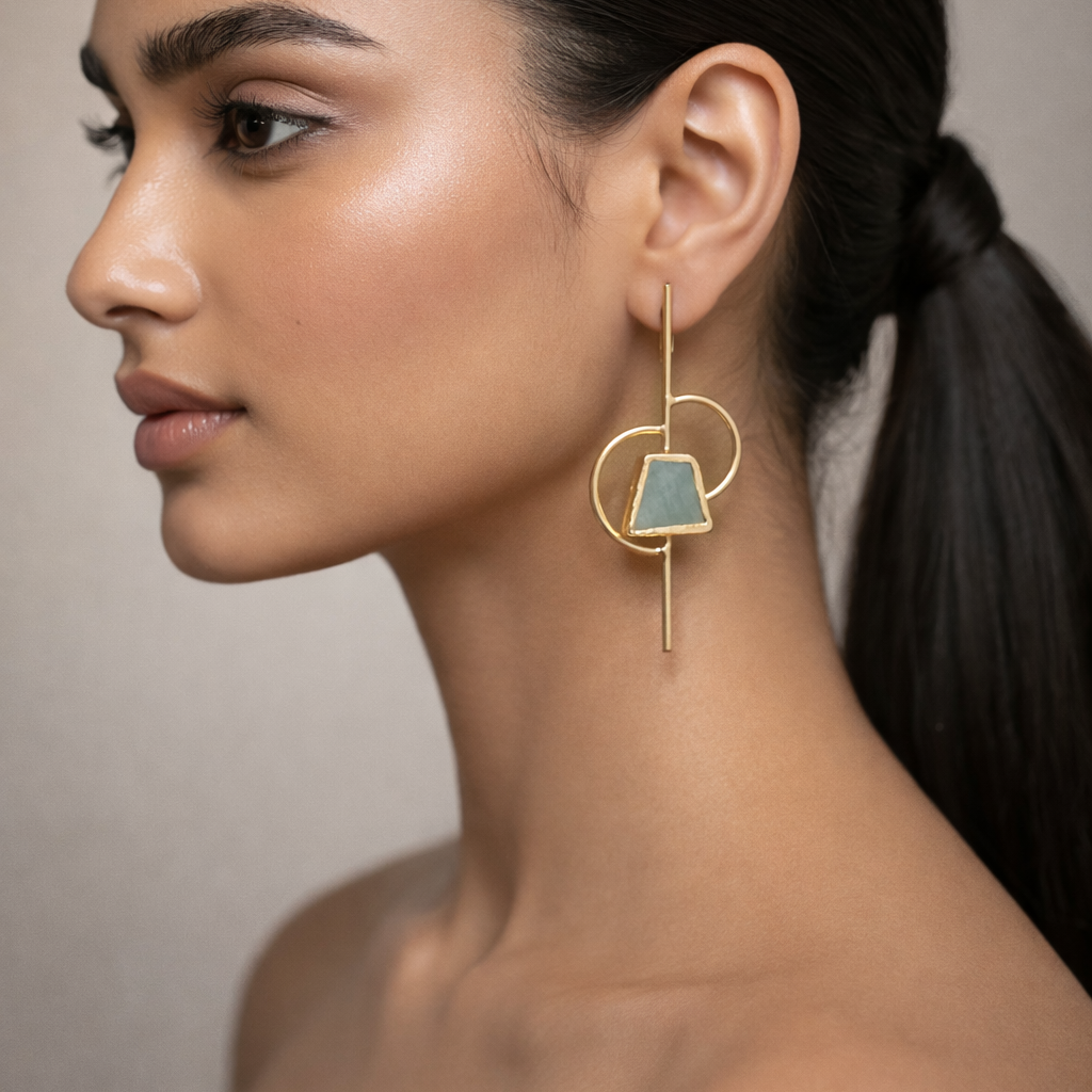 Woman wearing a gold earring with a blue gemstone against a neutral background
