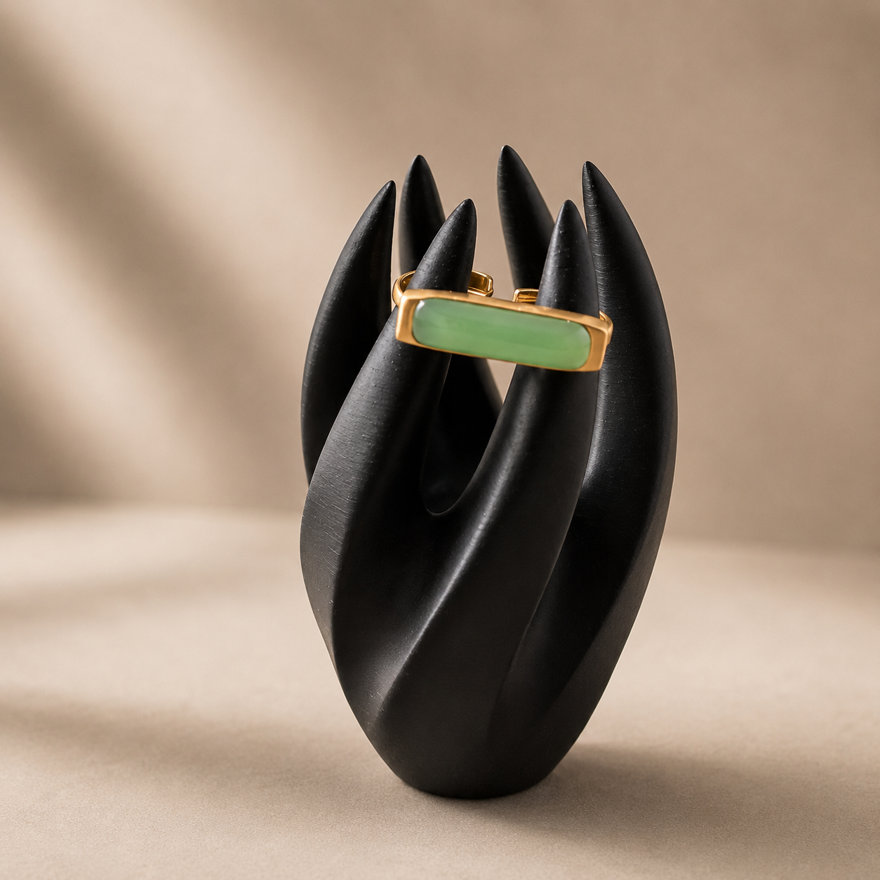Jewelry ring with green gemstone on a black ceramic stand against a beige background
