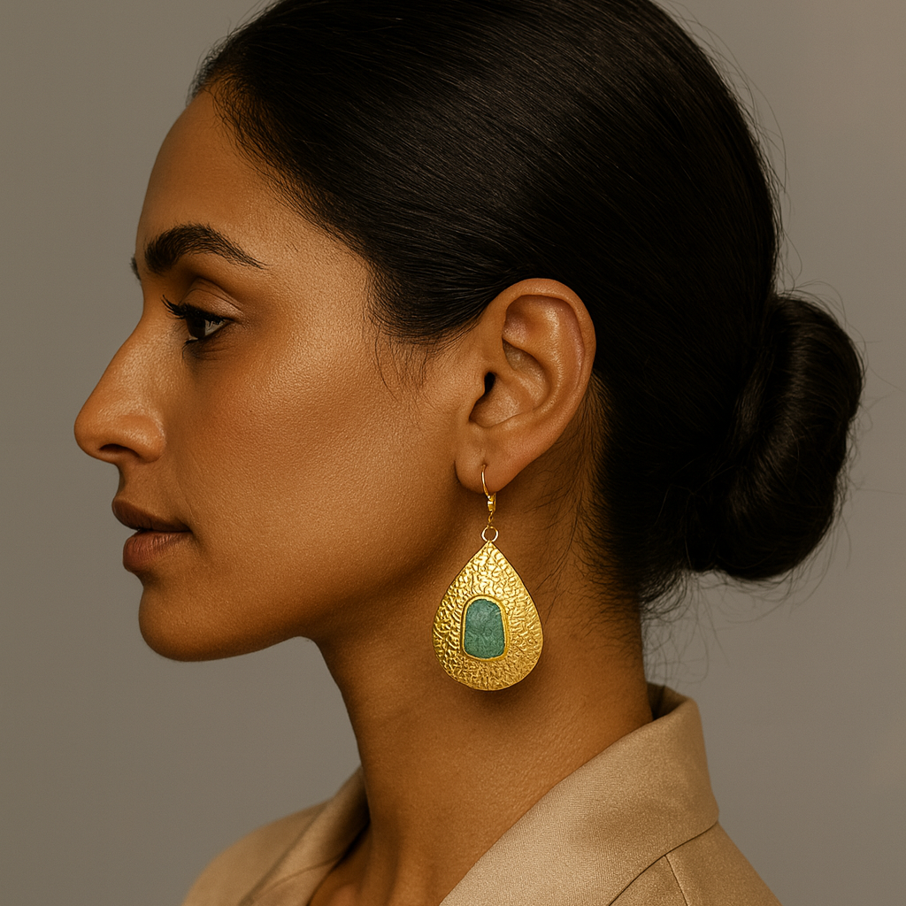 Woman wearing a gold earring with a green gemstone against a neutral background