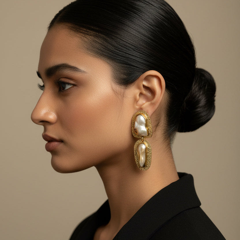 Woman wearing gold earrings with pearl-like stones against a neutral background
