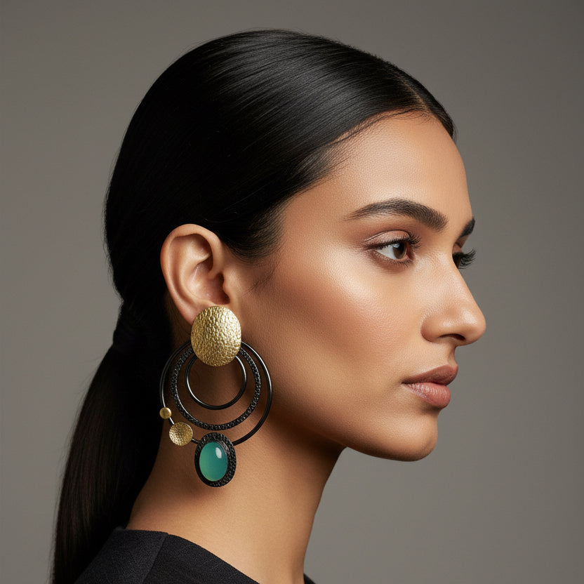 Pair of earrings with gold and silver circular designs on a black card against a dark fabric background