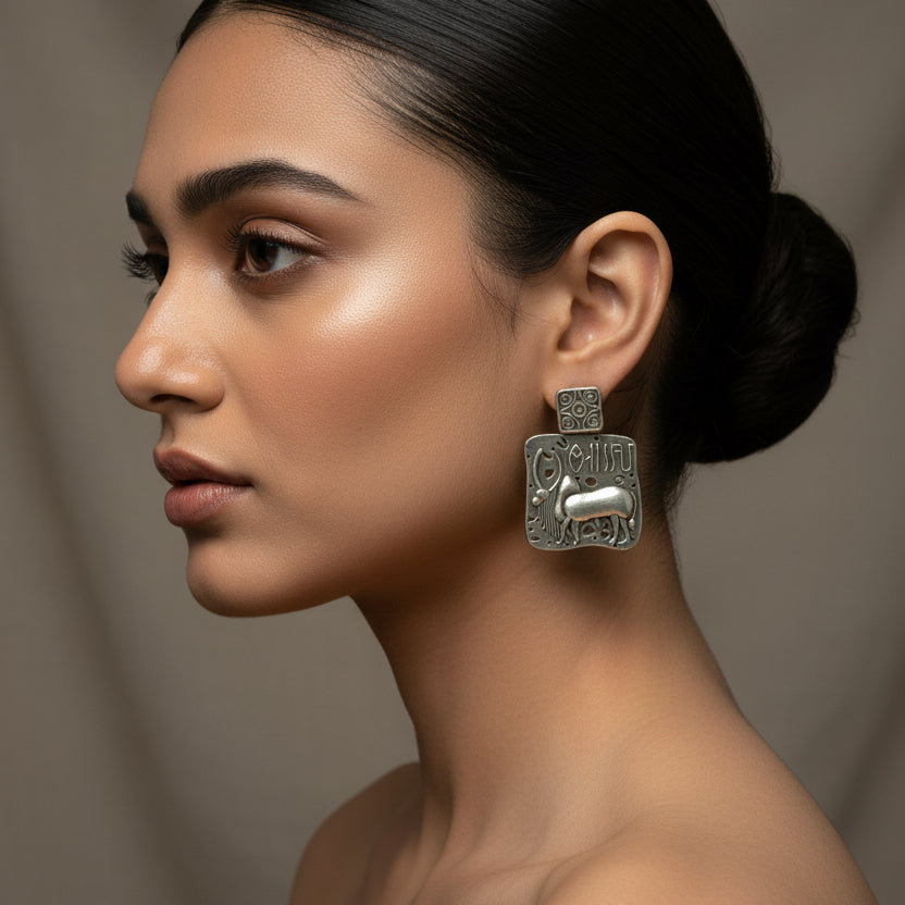 Pair of silver earrings with intricate designs on a black fabric background