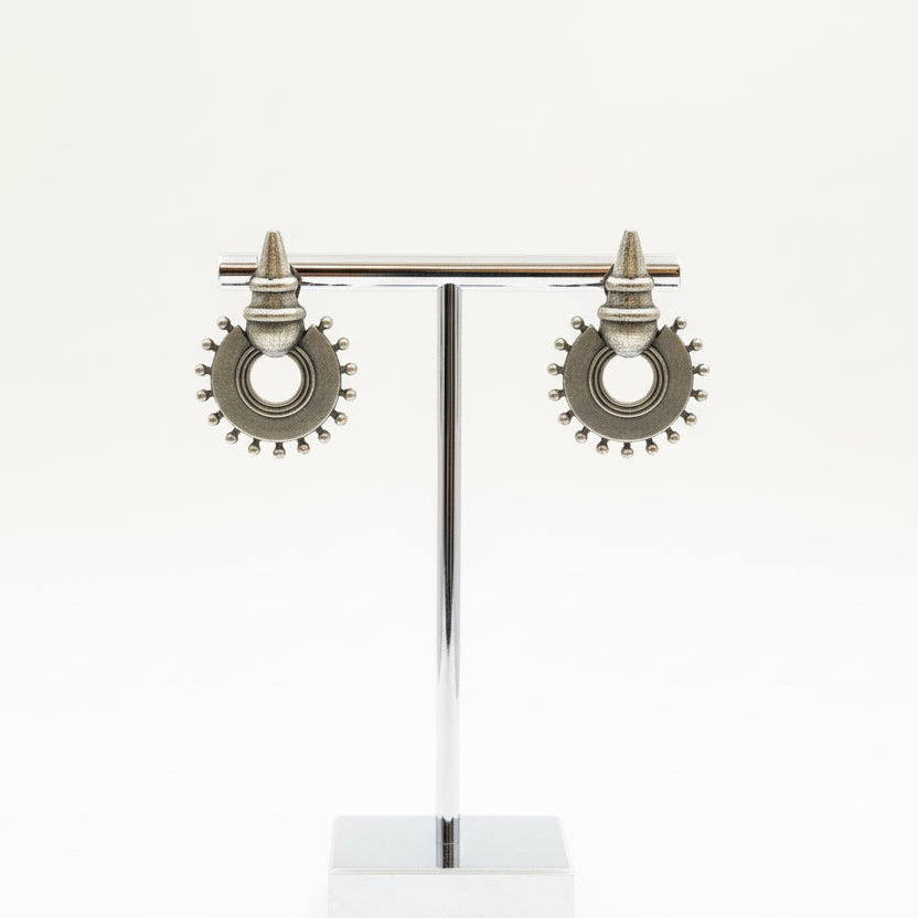 Pair of silver earrings on a stand against a white background