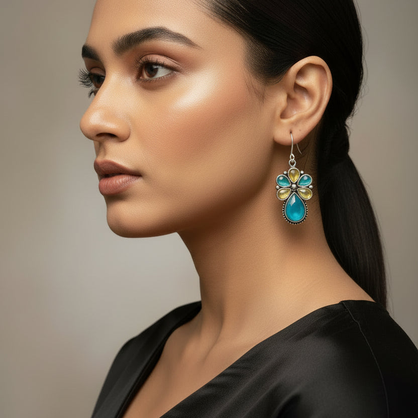 Pair of floral earrings with turquoise and yellow stones on a dark fabric background