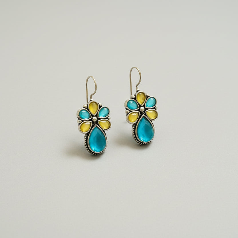 Pair of floral earrings with turquoise and yellow stones on a dark fabric background