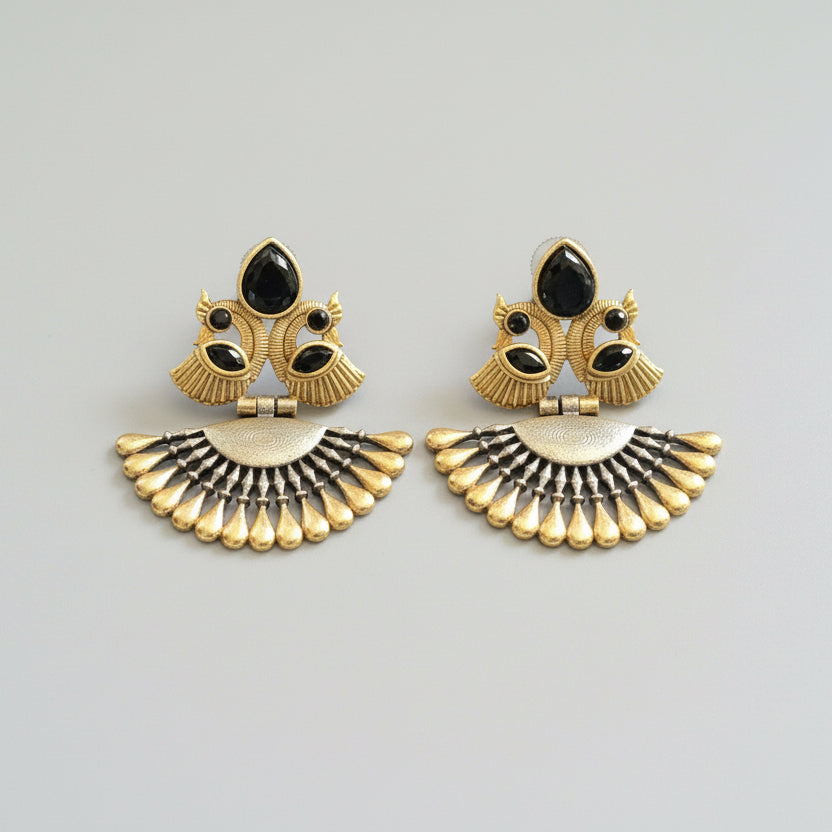 Pair of gold and black earrings on a gray fabric background