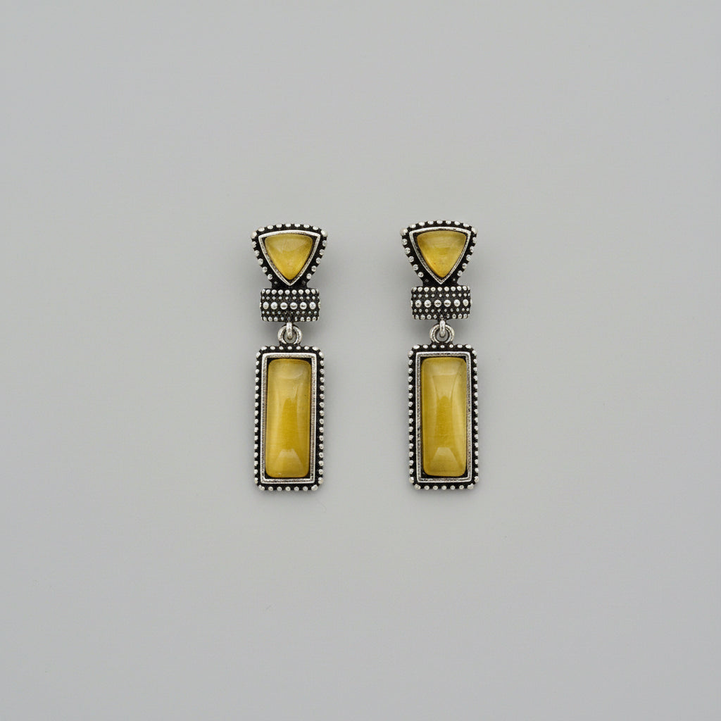 Pair of earrings with yellow stones and silver accents on a gray background