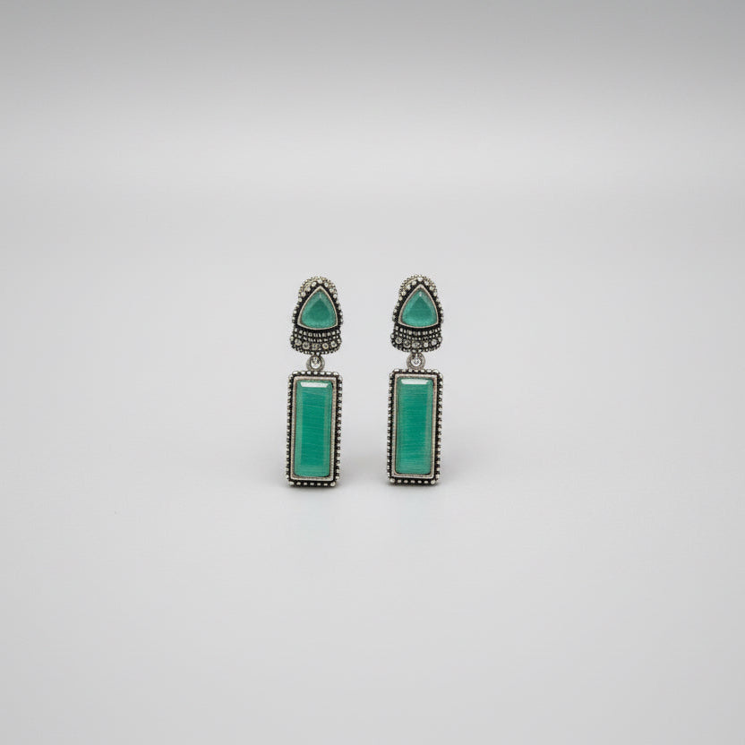 Pair of earrings with green gemstones on a gray background