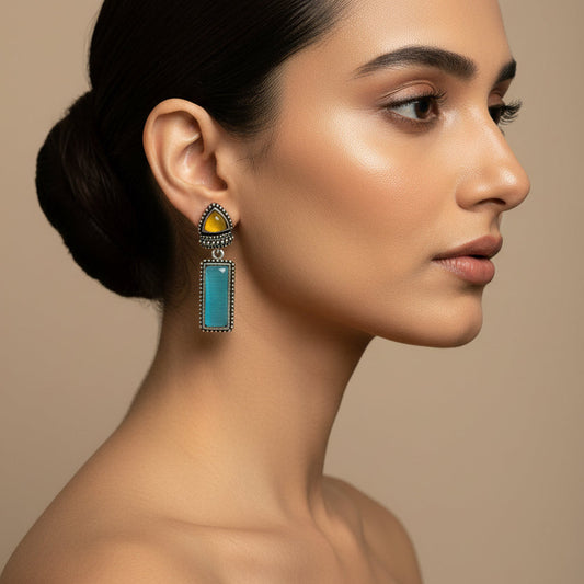 Pair of earrings with turquoise stones and yellow accents on a dark fabric background