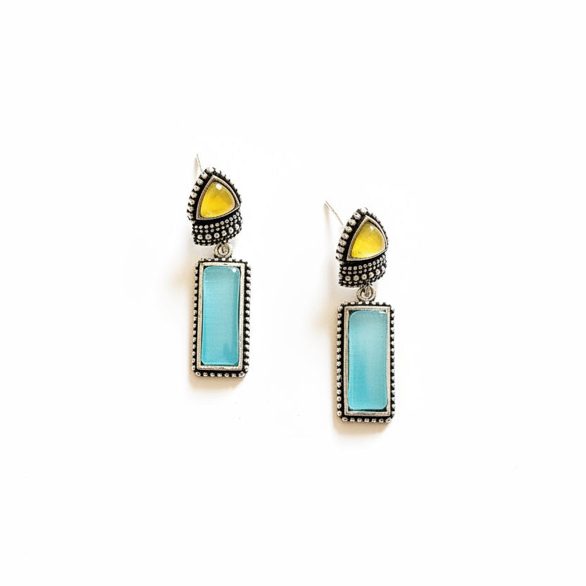 Pair of earrings with turquoise stones and yellow accents on a dark fabric background