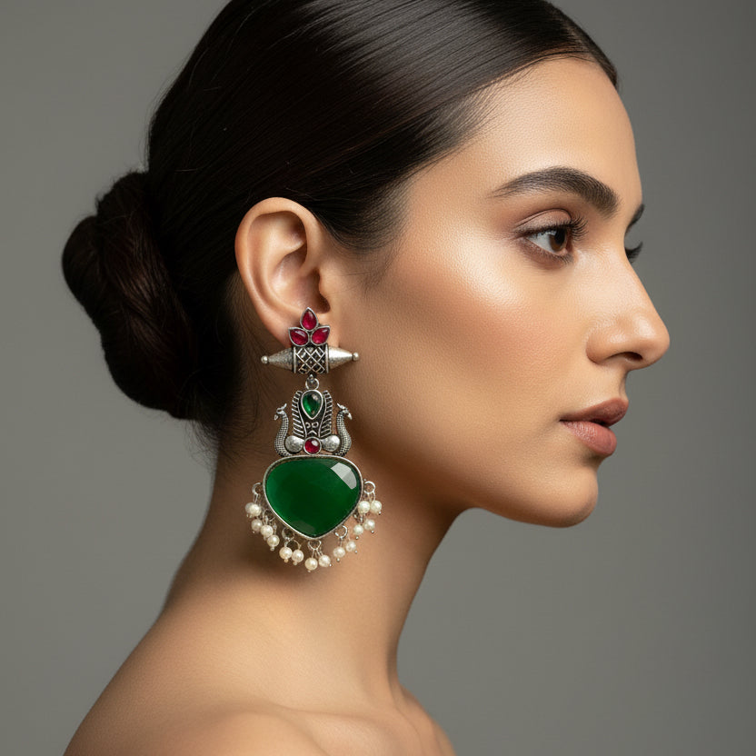 Pair of green heart-shaped earrings with silver and red accents on a black fabric background