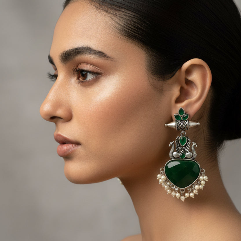 Pair of green heart-shaped earrings with silver and green accents on a black fabric background