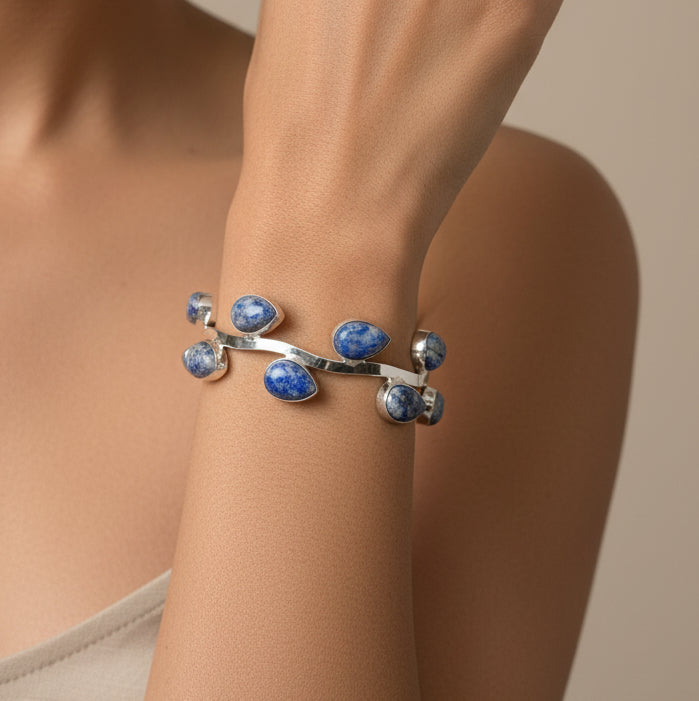 Silver bracelet with blue stones on a wrist against a black and green background
