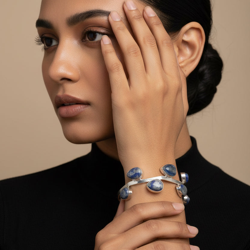 Silver bracelet with blue stones on a wrist against a green and black background