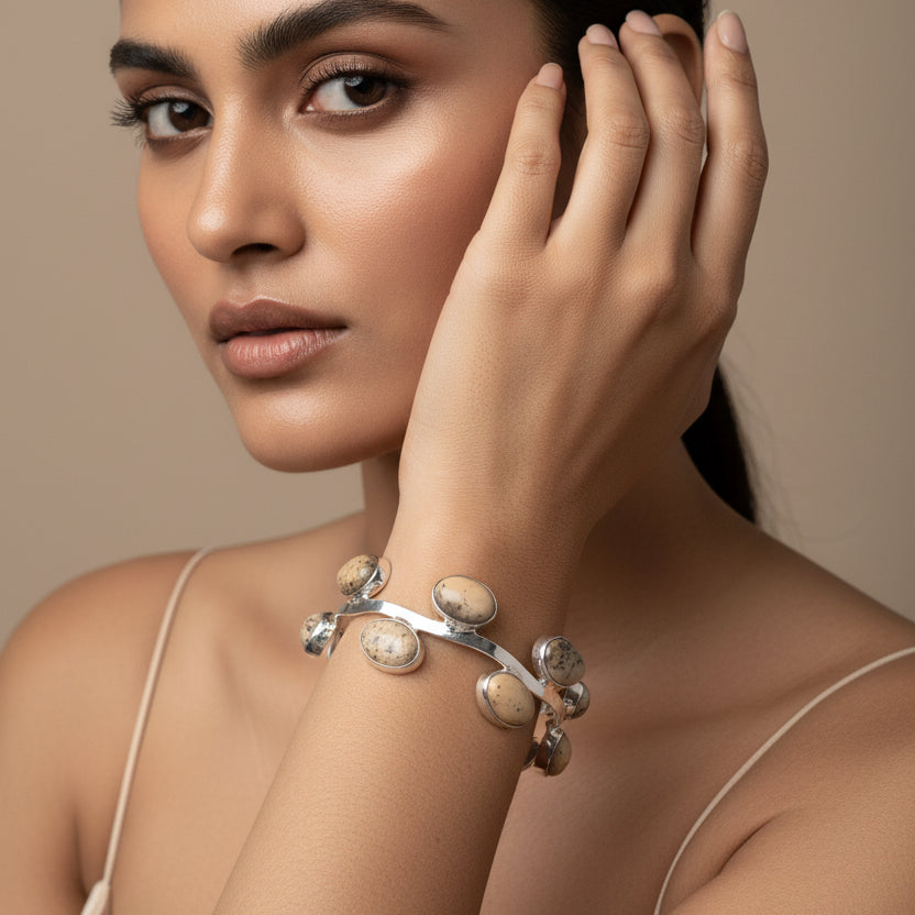 Close-up of a hand wearing a silver bracelet with round embellishments on a striped fabric background.