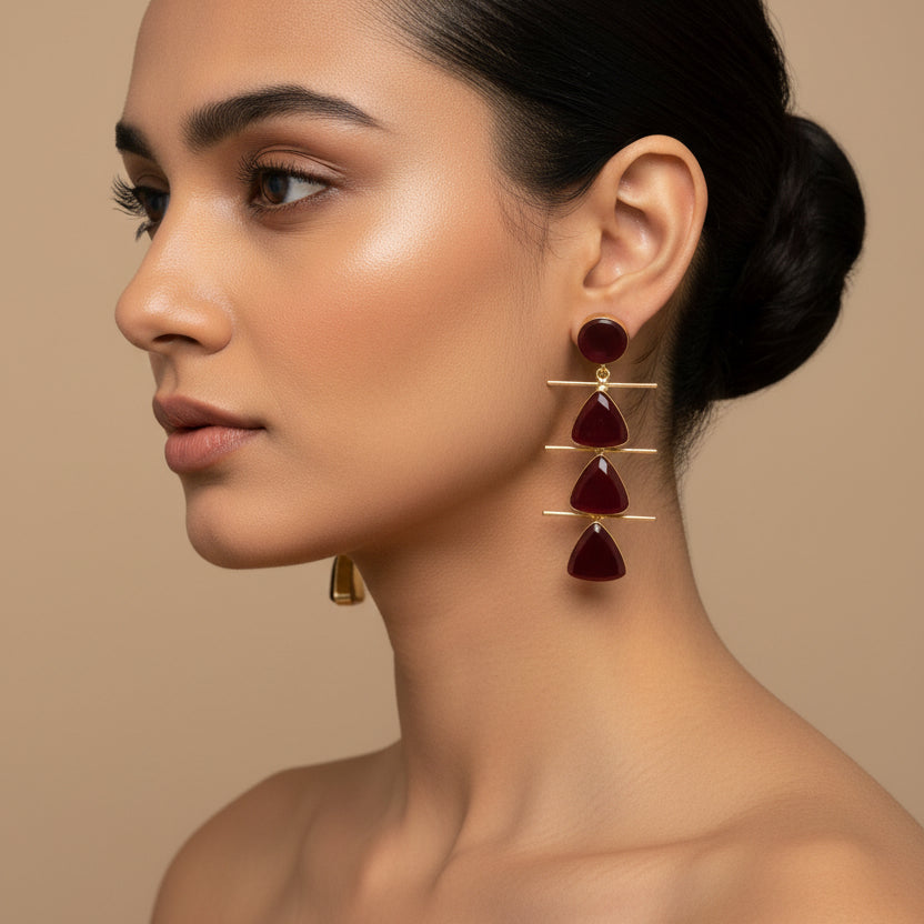 Pair of earrings with gold and red design on a dark surface