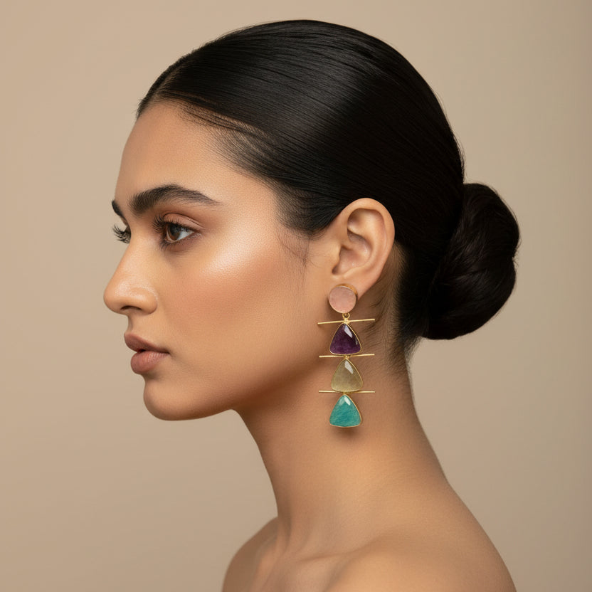 Pair of brass earrings with triangular gemstones on a dark background
