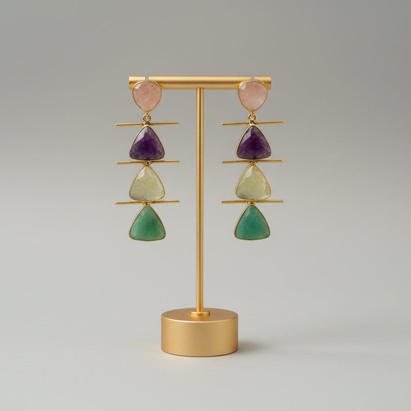 Gold earring stand with colorful gemstone earrings on a gray background