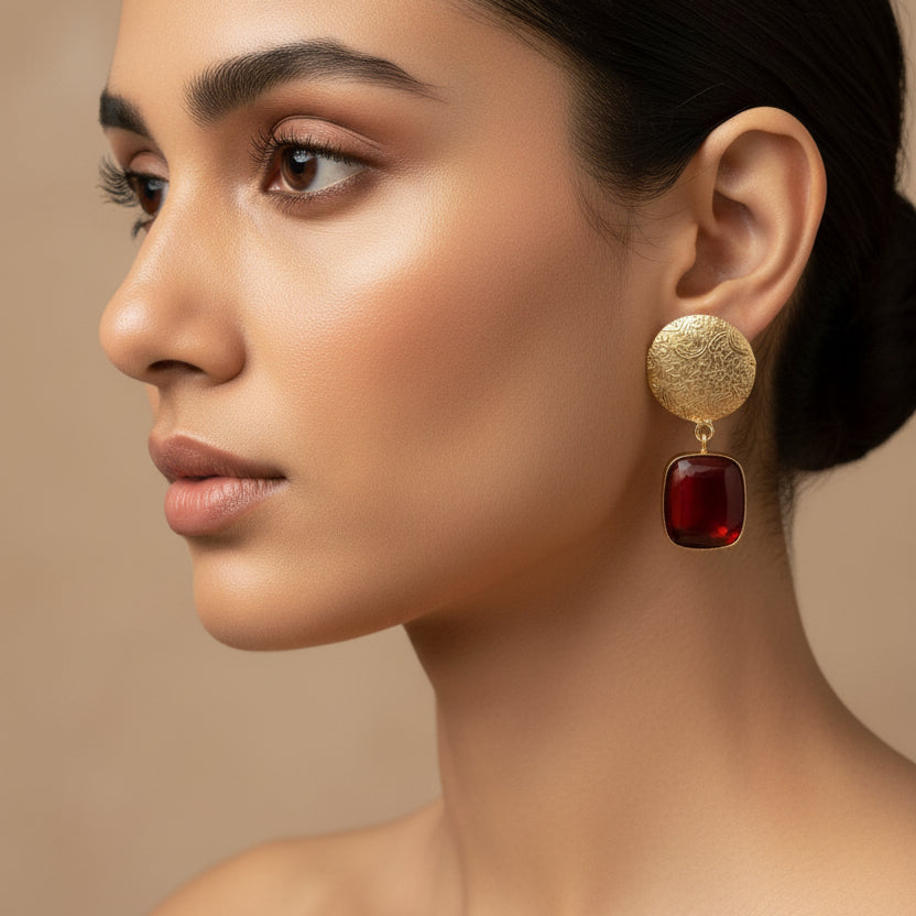 Pair of gold earrings with red stones on a black surface