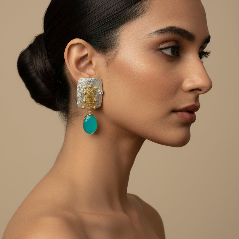 Pair of earrings with gold and turquoise design on a black surface