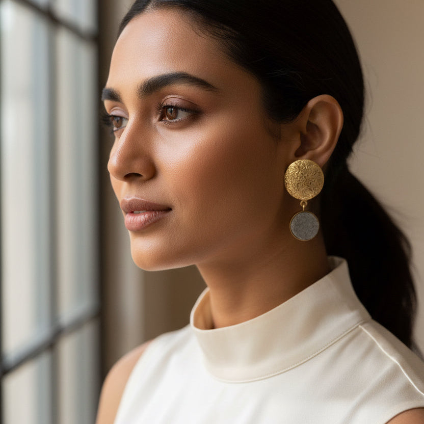 A pair of vintage gold-toned dangle earrings with textured oval top plates and round gray stone or enamel drop pendants, displayed on a solid black background.