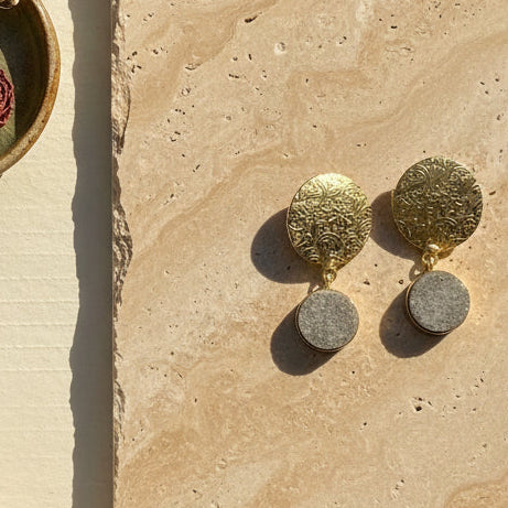 A pair of vintage gold-toned dangle earrings with textured oval top plates and round gray stone or enamel drop pendants, displayed on a solid black background.