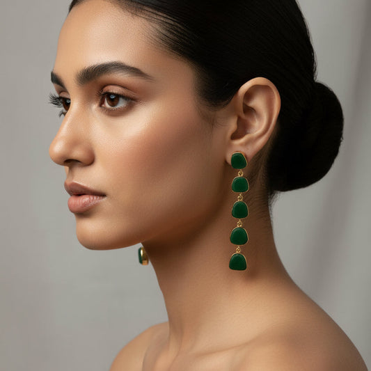 A pair of gold drop earrings with five irregular dark green stone charms, displayed on a black textured fabric background.