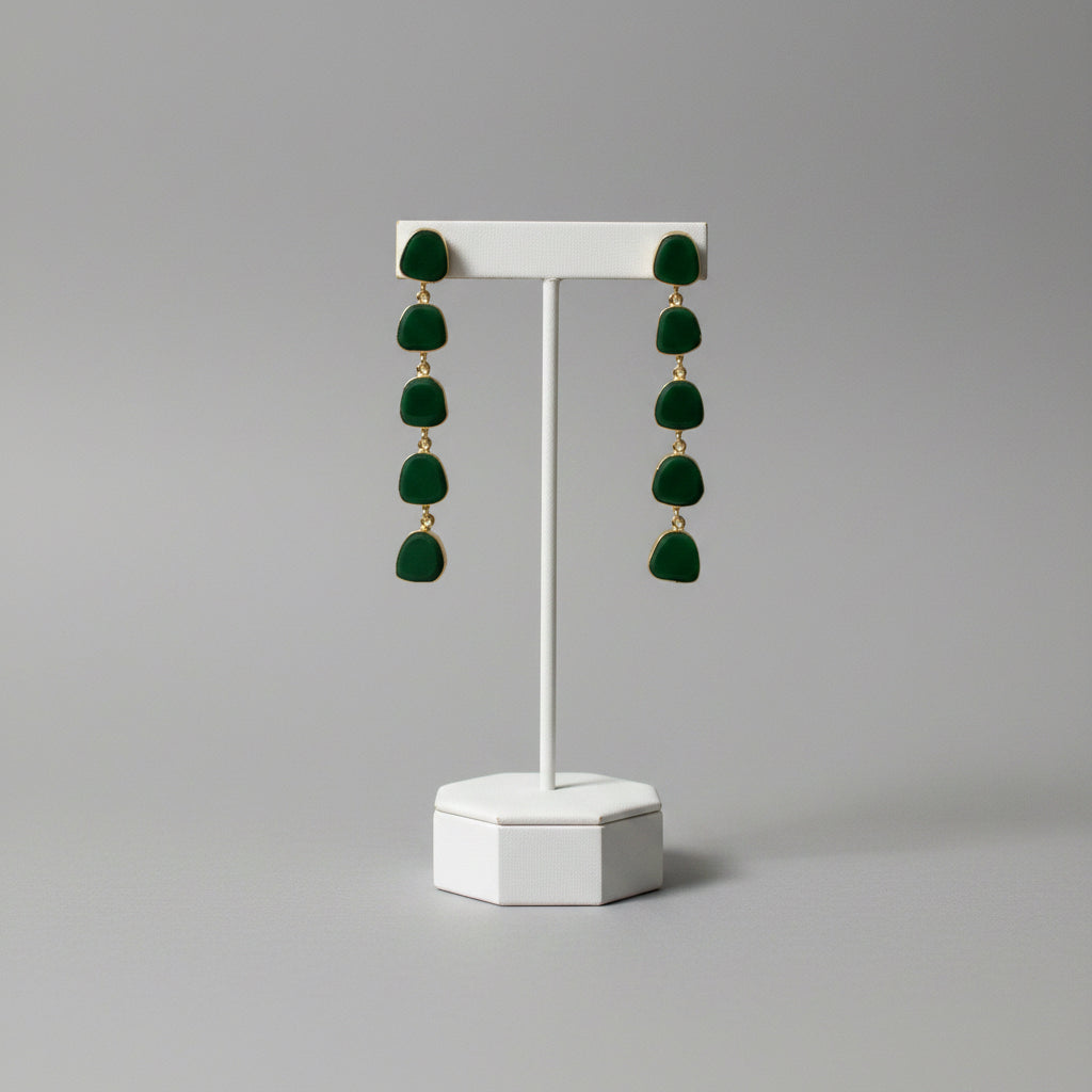 A pair of gold drop earrings with five irregular dark green stone charms, displayed on a black textured fabric background.