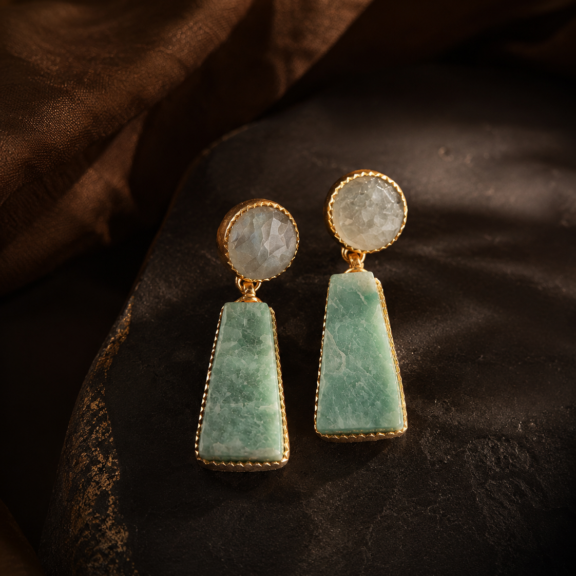 Pair of earrings with greenstone and gold accents on a dark fabric background