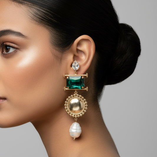 Ornate earrings with green gemstones and pearl-like elements on a dark background
