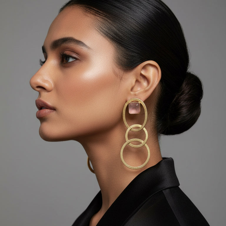 Gold hoop earrings with pink gemstones on a black card, placed on a textured surface.