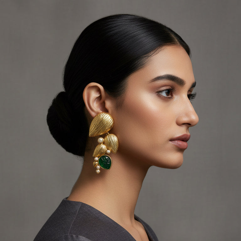 Gold and green earrings with pearls on a black card against a textured beige background