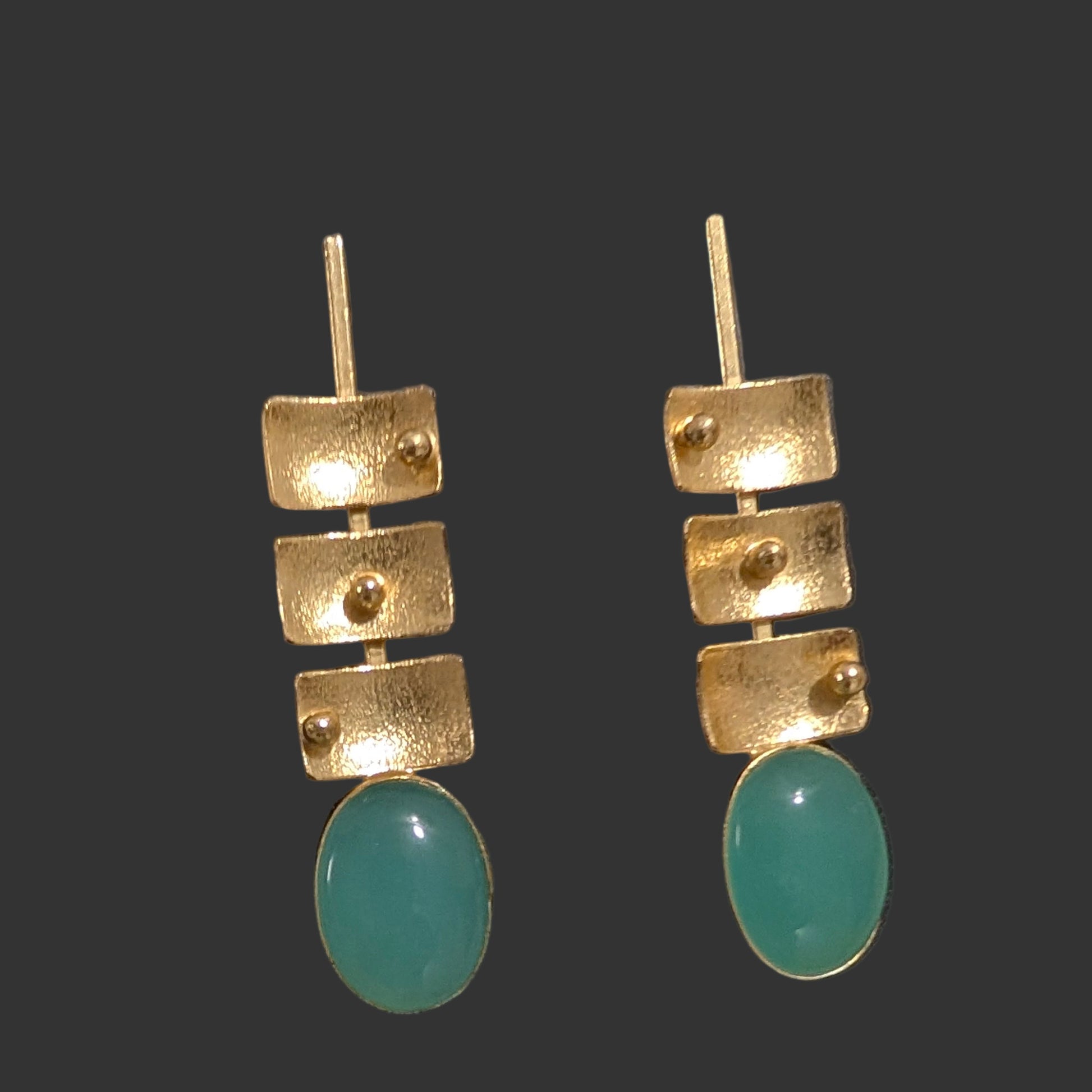 Gold and turquoise earrings on a black card with a textured gray background