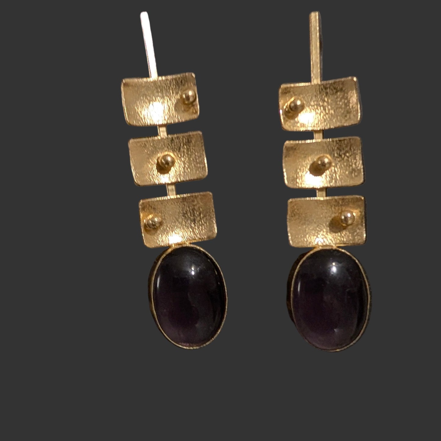 Pair of gold and purple earrings on a black card with a textured gray background