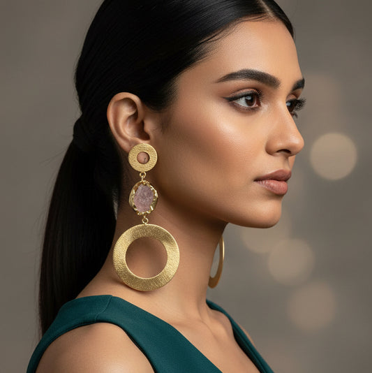 Gold hoop earrings with pink gemstones on a gray card against a dark background