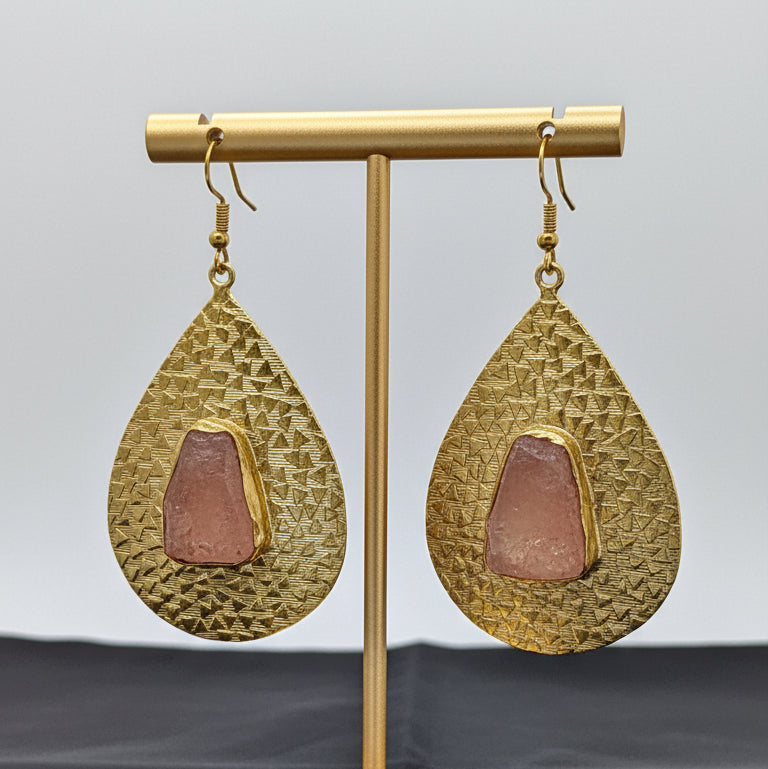Gold teardrop earrings with embedded pink stones on a black background