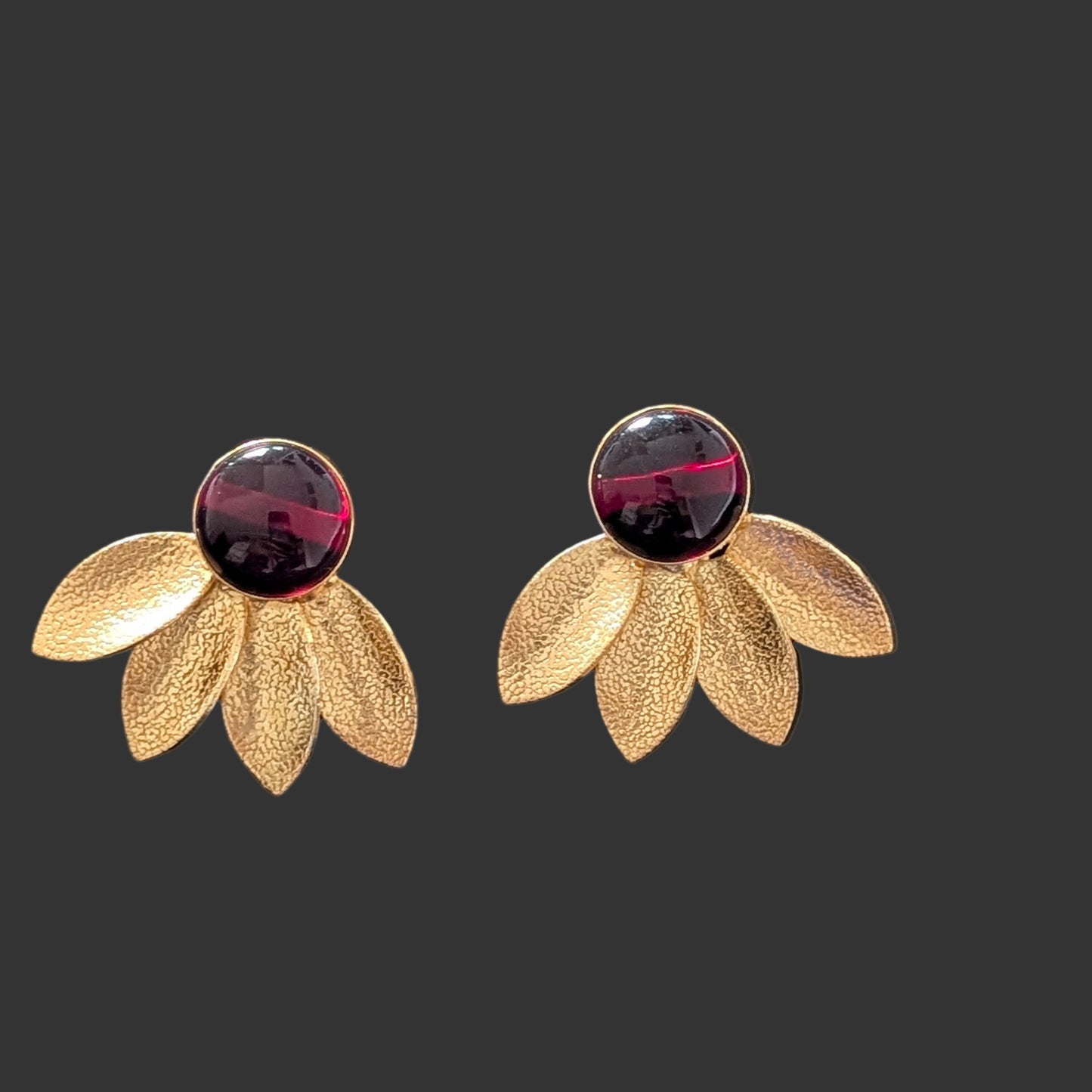 Gold flower-shaped earrings with purple gemstones on a black card against a dark background