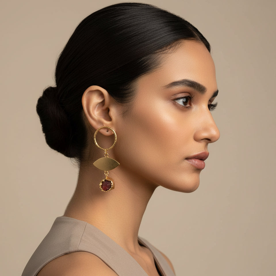 Gold earrings with circular top and leaf-shaped pendant on a black background